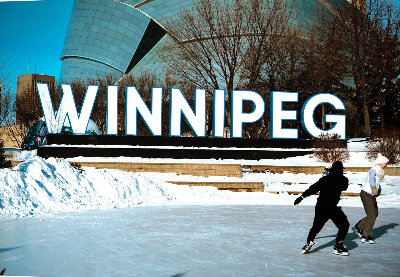People ice skating in front of the iconic Winnipeg sign on a sunny winter day.