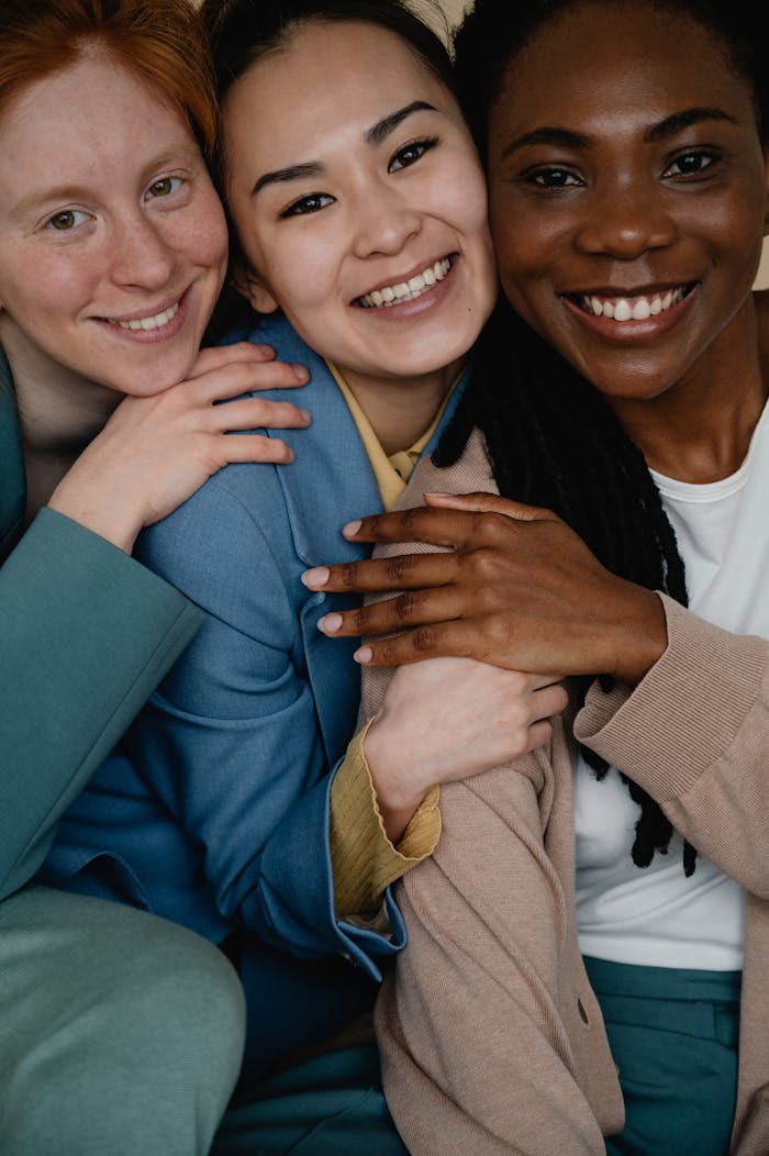 Three diverse women smiling and embracing, symbolizing friendship and unity.